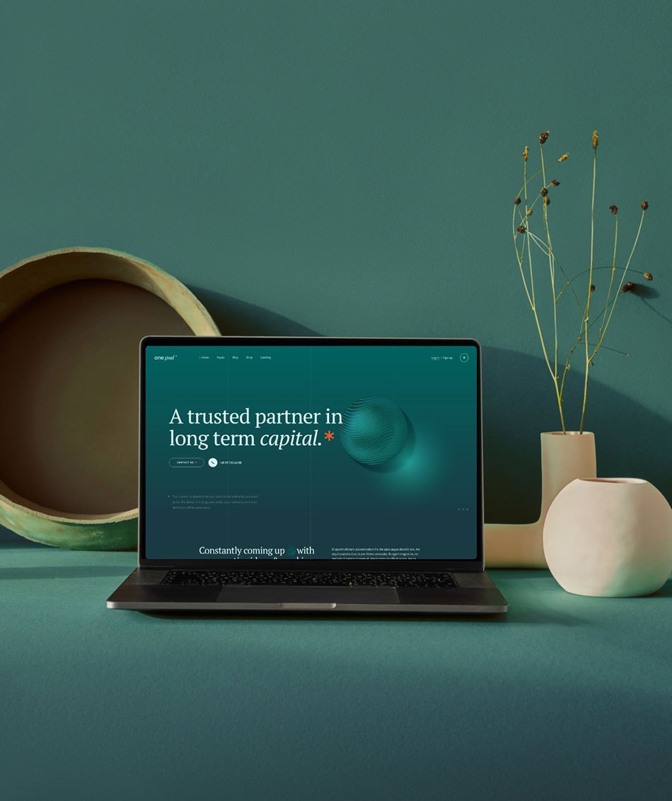 A laptop displaying a website with the text "A trusted partner in long term capital" is on a green surface. It is surrounded by minimalist ceramic vases, one round and the other tall with dried flowers, all set against a green backdrop.